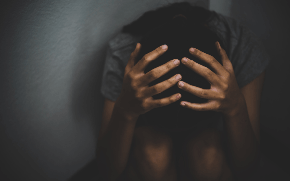 Pessoa com a cabeça entre as mãos em um ambiente escuro, representando tristeza profunda e depressão.