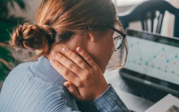 Mulher com dor no pescoço trabalhando em frente ao computador, simbolizando estresse, tensão emocional, ansiedade e impactos da saúde mental no ambiente profissional.